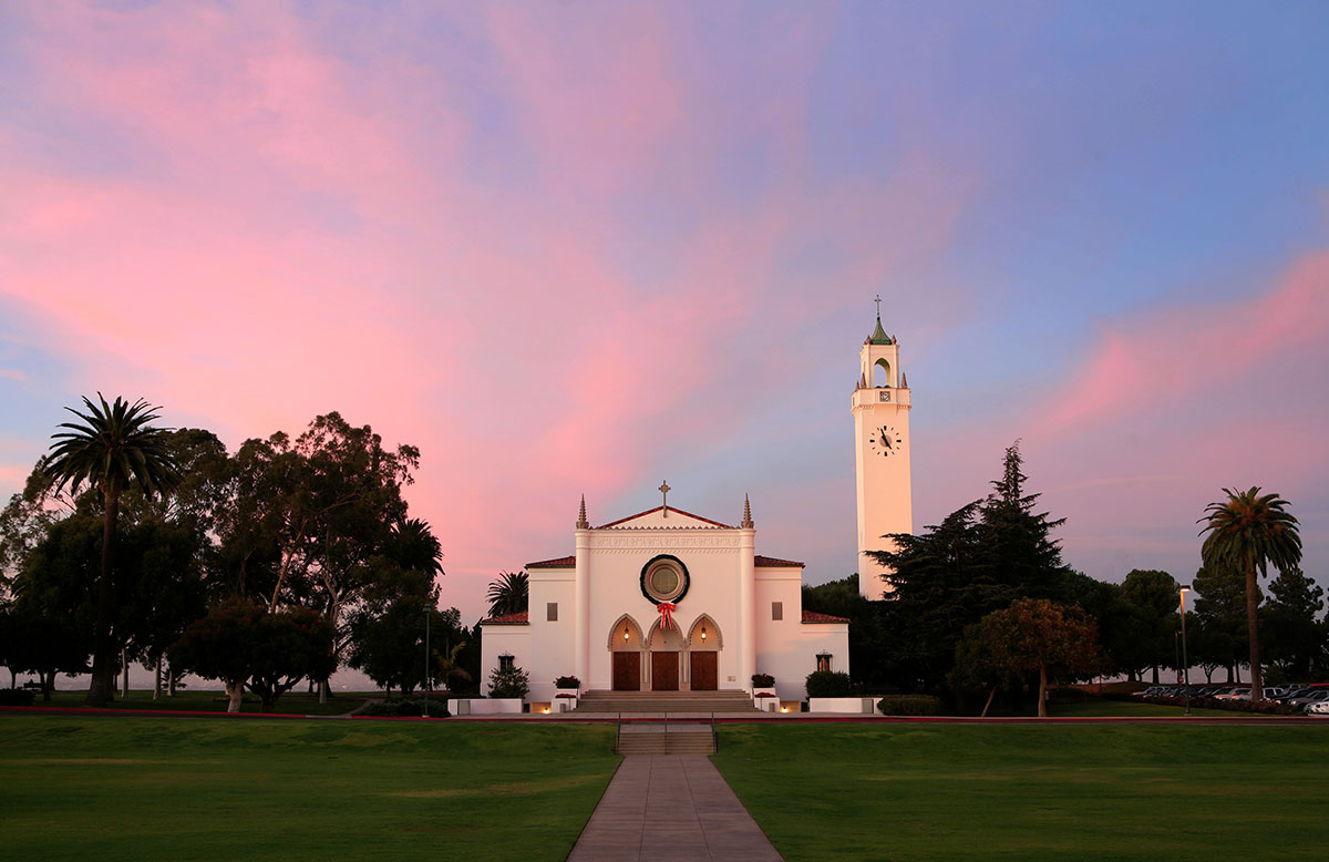 Sacred Heart Chapel with a wreath over the front door and a colorful sky at sunset