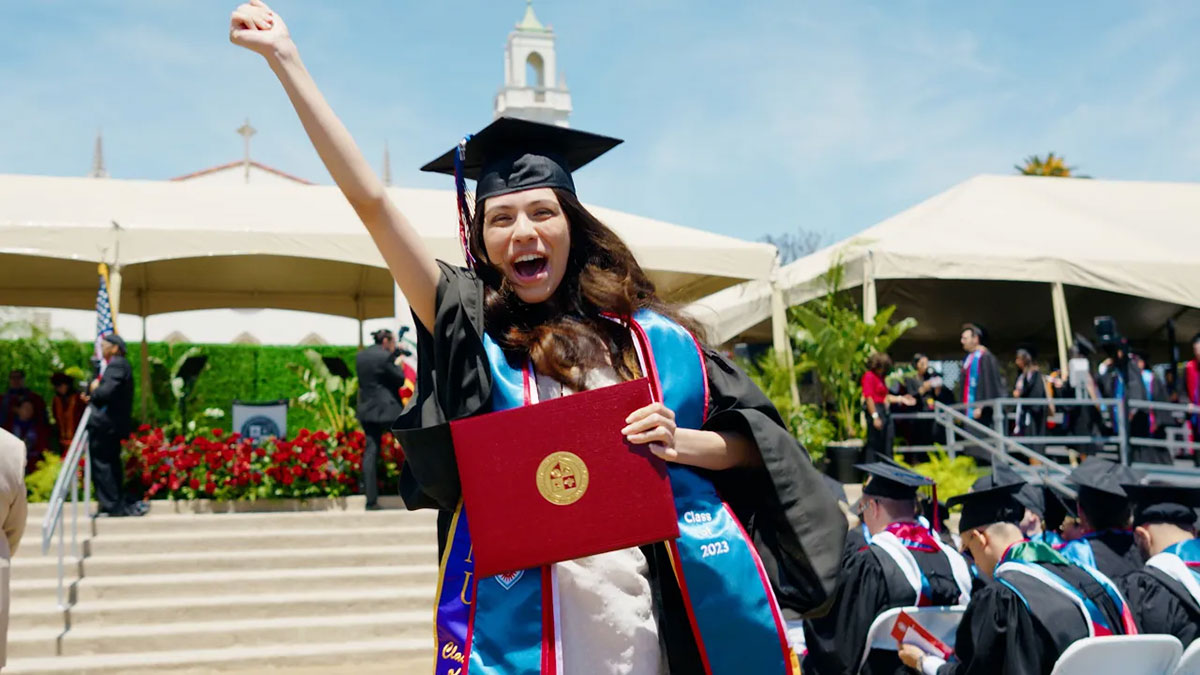 A graduate walking off the stage with their diploma with their hand raised in the air in triumph