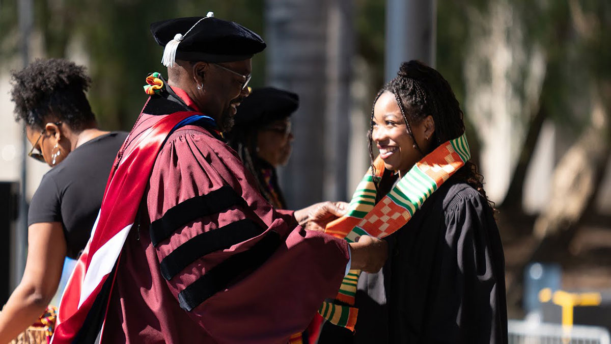 A faculty member draping a sash over a graduating student's shoulders