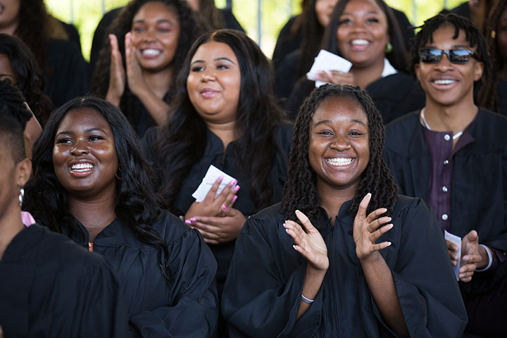 Students smiling and clapping along with other graduates wearing their cap and gowns