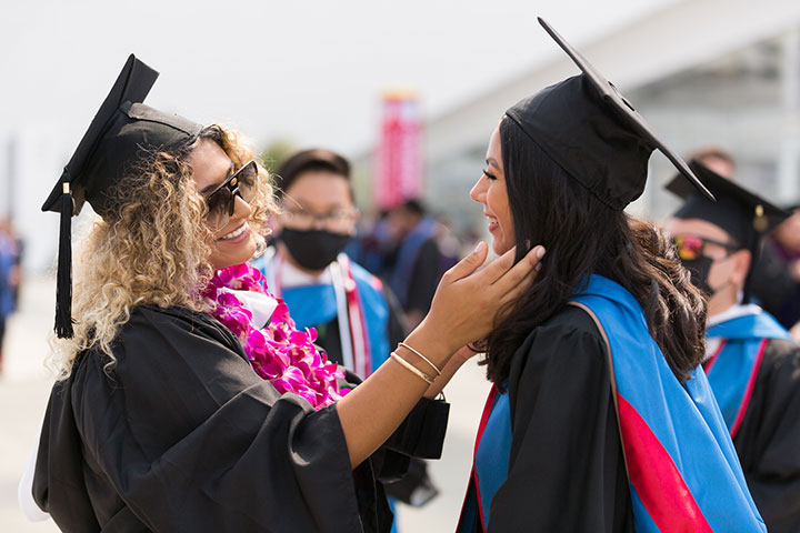 A graduate being congratulated by a faculty member, both of whom are wearing graduation gowns
