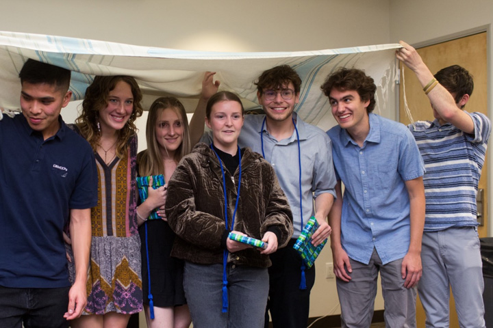 Students celebrating graduation in the Jewish tradition of holding a tallit overhead, which is a type of blanket that has symbolic significance in rituals and as a form of covering and protection