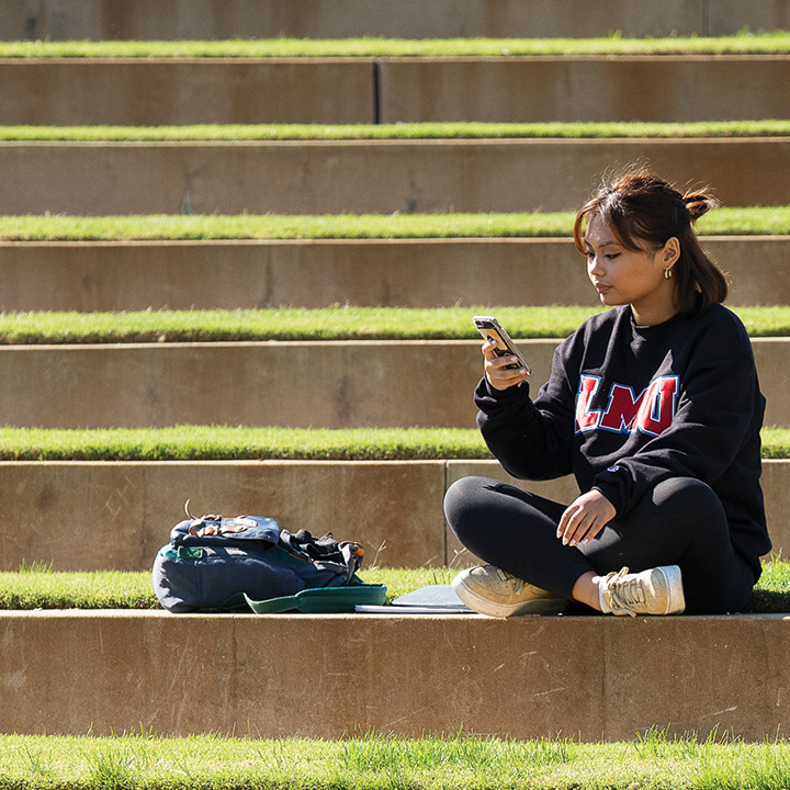LMU student checking phone on grass steps